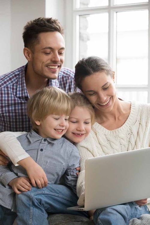 A family is sitting on the floor looking at a laptop computer.