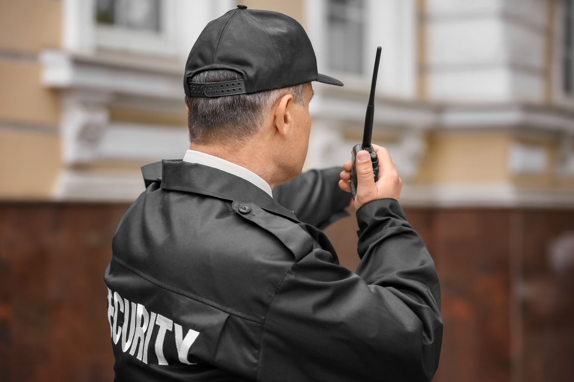 Security guard in black uniform using a walkie-talkie outdoors near a building Security guard in black uniform using a walkie-talkie outdoors near a building