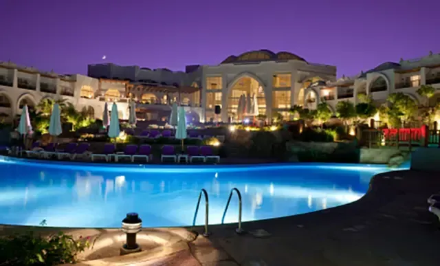 A large swimming pool is lit up at night in front of a large building.