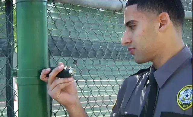 A security guard is holding a key to a chain link fence.