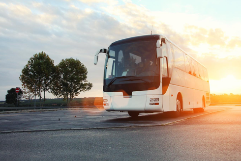 A white coach bus parked on an asphalt lot at sunset, with trees in the background.
