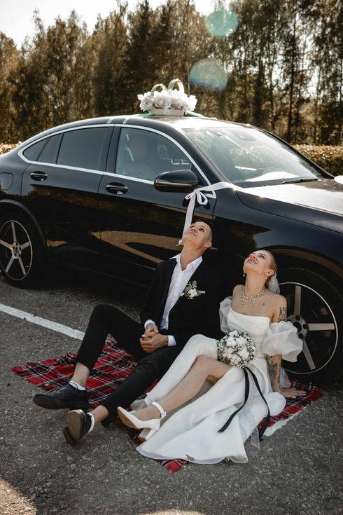A bride and groom in formal wedding attire look at each other while seated together in the back of a limousine.