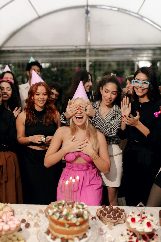 Five people pose and hold drinks with pink balloons in a festive limousine setting.