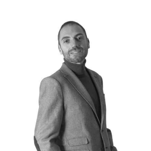 Hombre con blazer y cuello alto, sonriendo, delante de un fondo blanco.