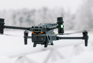 Grey drone in flight against a blurred snowy background.