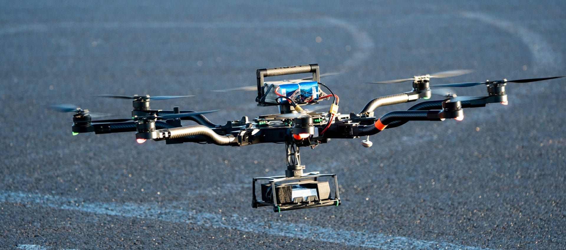 Drone flying over asphalt with camera attached.
