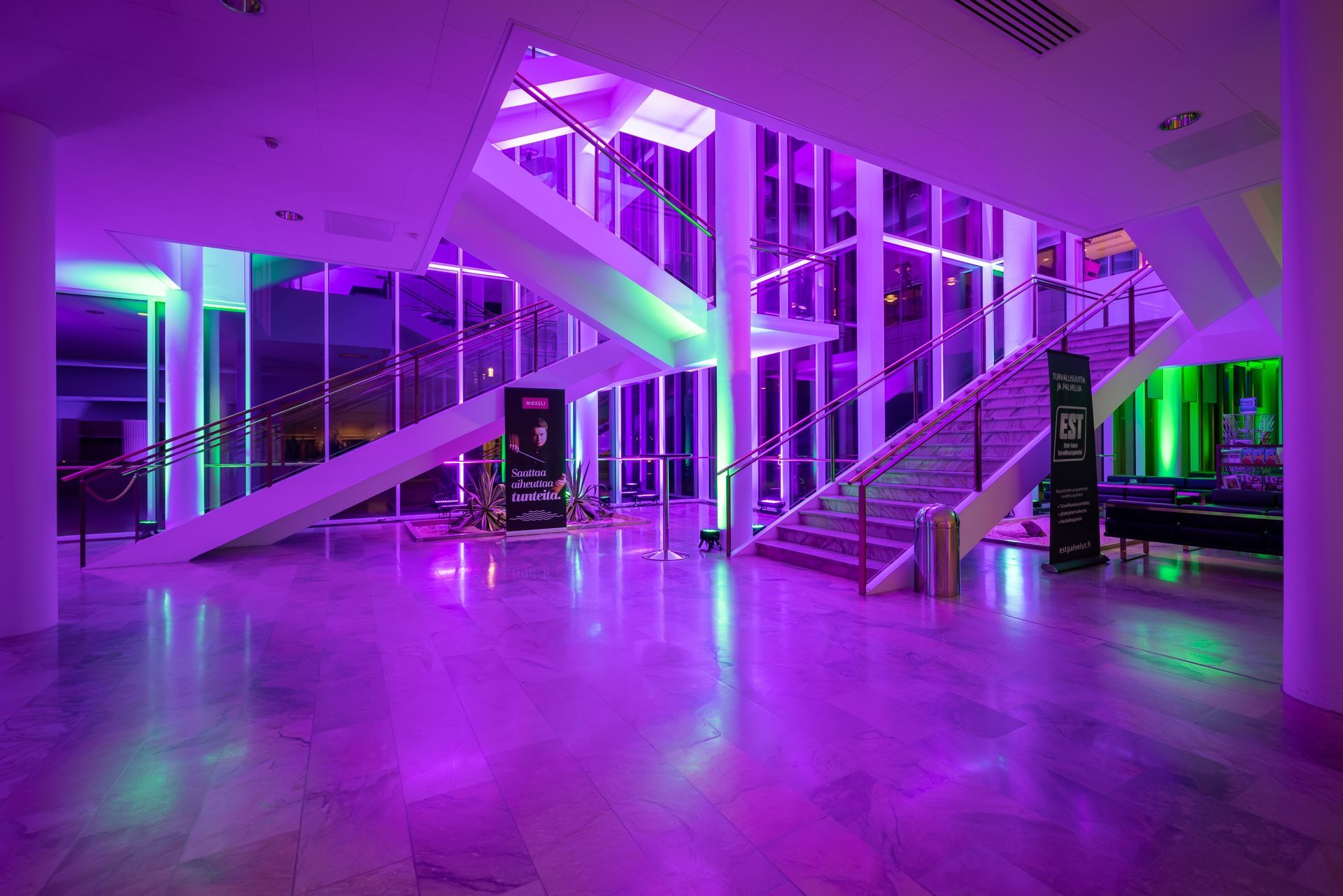 Spacious lobby with marble floor and purple lighting; stairs and glass walls visible.