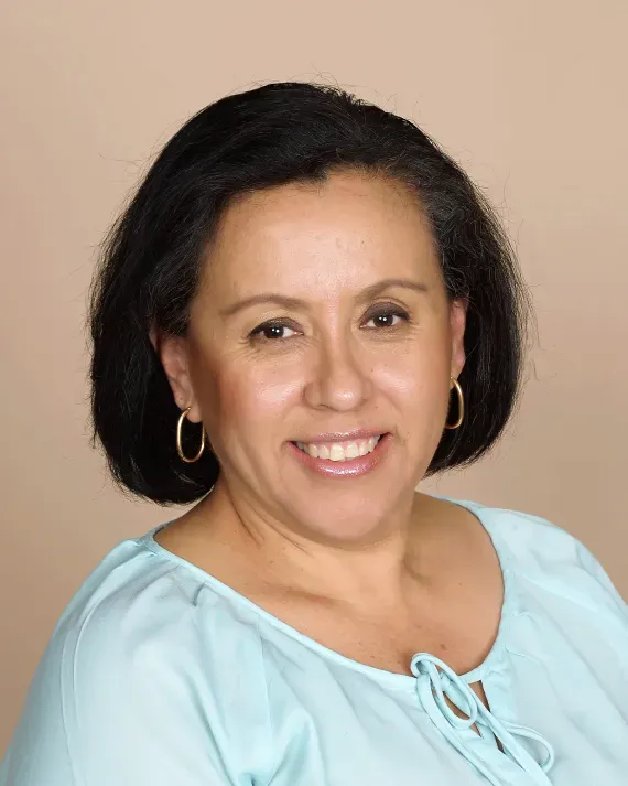 Portrait of a smiling woman in a light blue blouse against a beige background