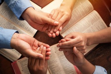 Hands joined in a circle over an open book, suggesting teamwork or prayer