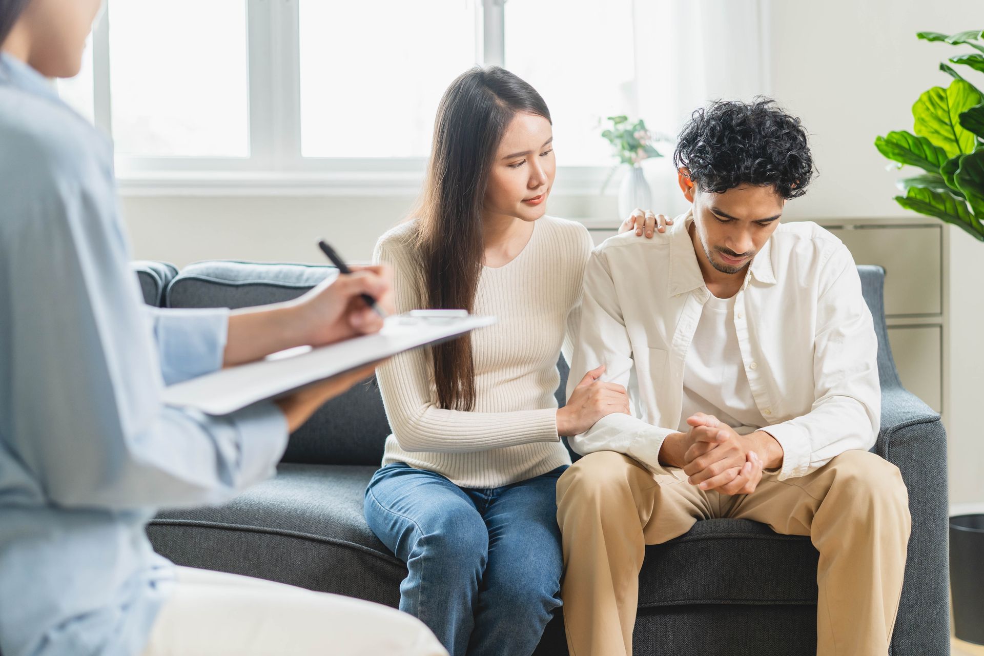 Counselor talks with a seated couple on a sofa in a bright living room.