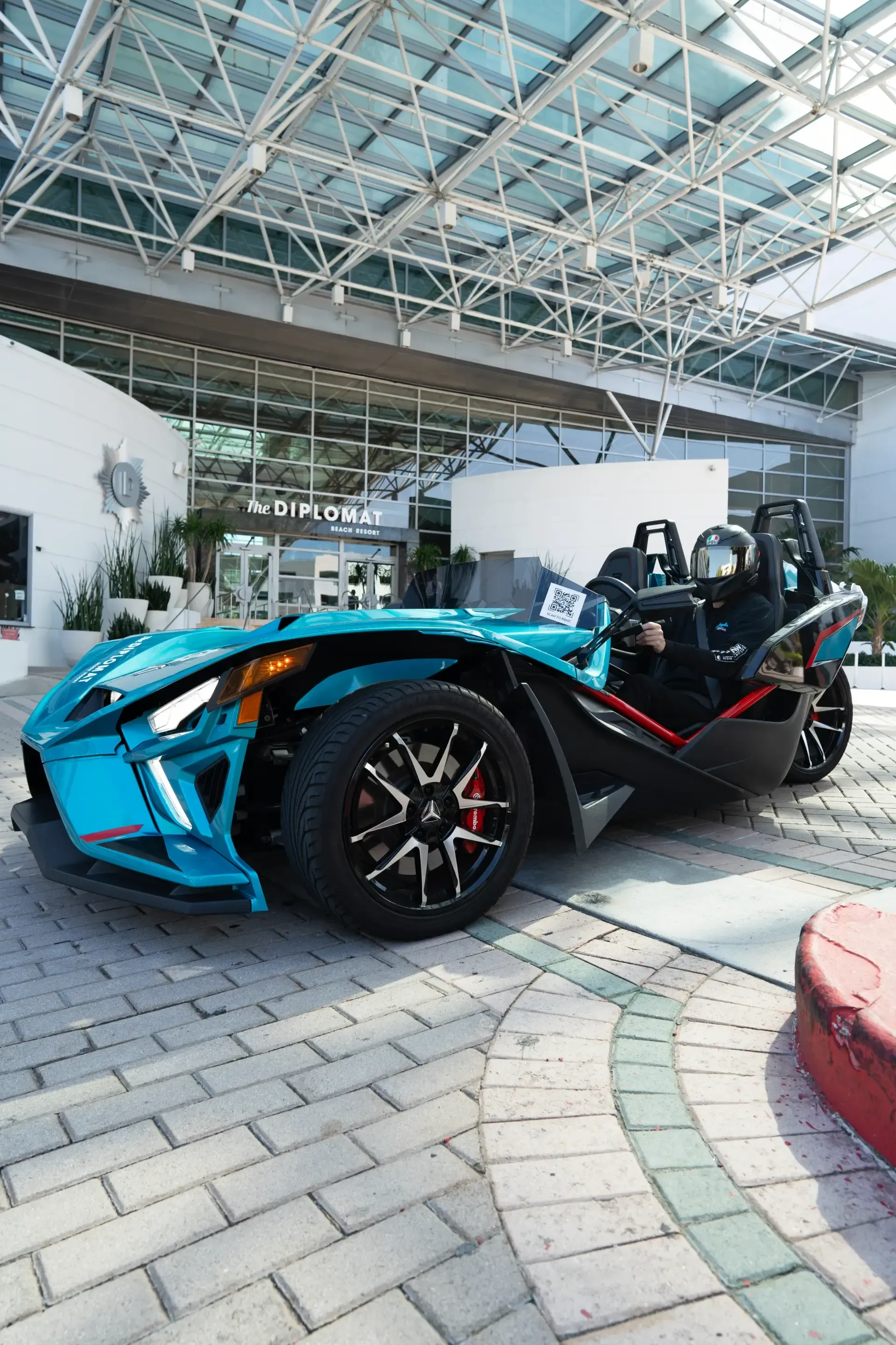 Two people are riding in a blue slingshot on a city street.
