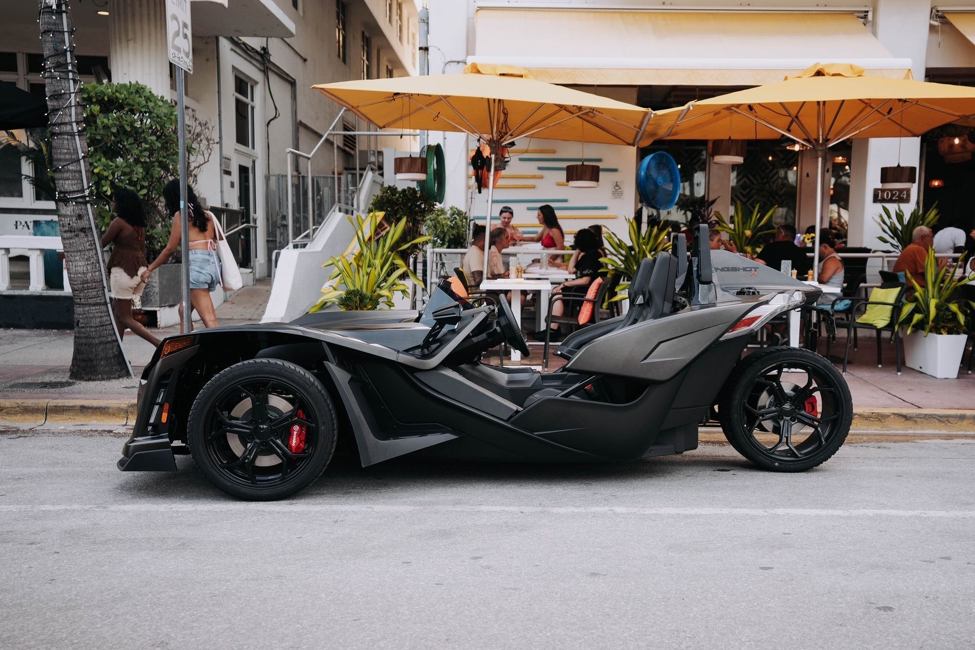 A slingshot is parked in front of a tall building.