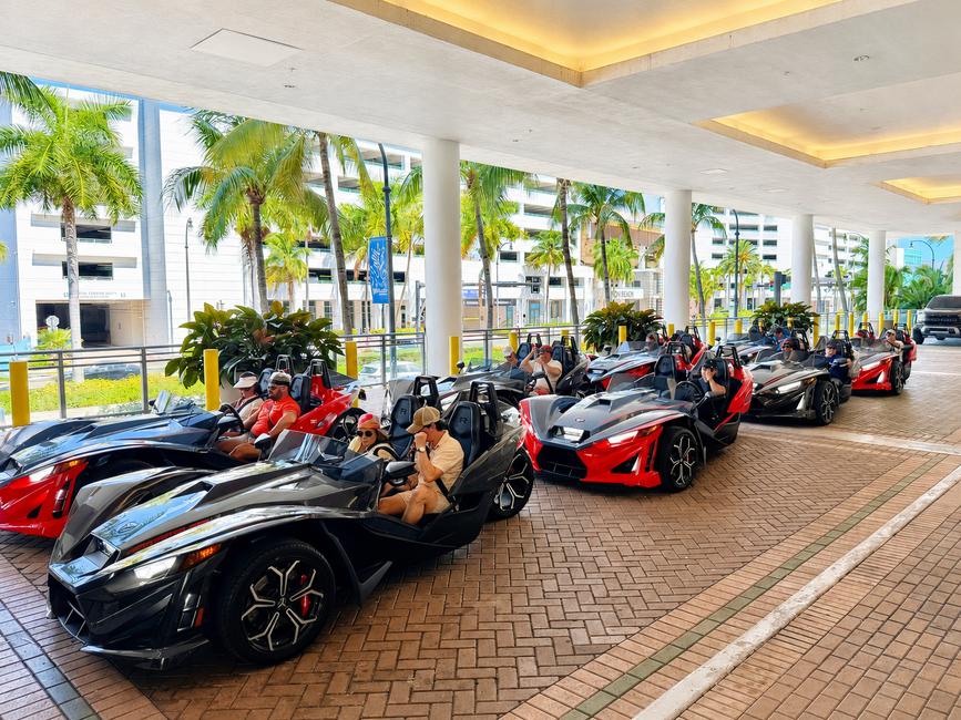 A line of red and black Polaris Slingshots parked under a covered hotel entrance.