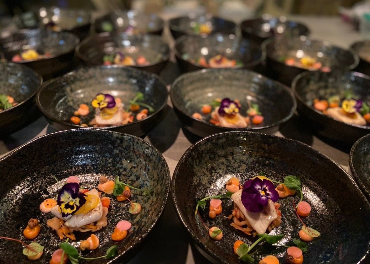 Luxe amuse met vis en eetbare bloemen geserveerd in zwarte keramieken schalen