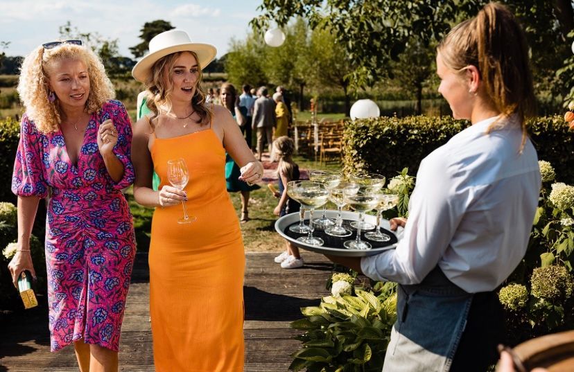 bediende serveert champagne aan dame in oranje jurk