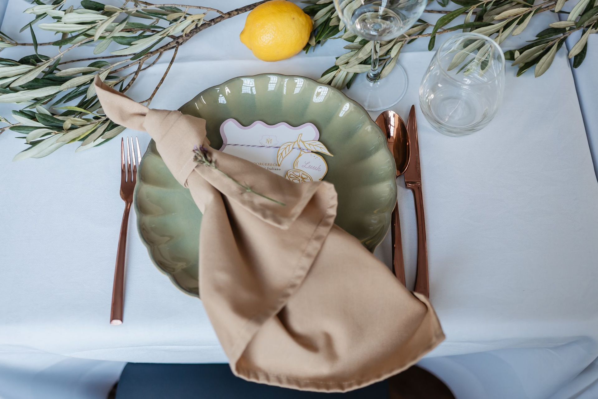 Een feestelijk gedekte tafel met een wit tafelkleed, voorzien van naamkaartjes, waaronder één met de naam 