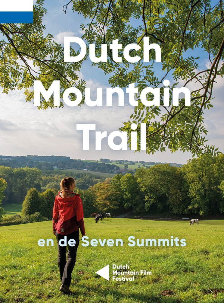 Vrouw wandelend op een groene heuvel, bordje van de Nederlandse Bergroute. Weelderig landschap met bomen.