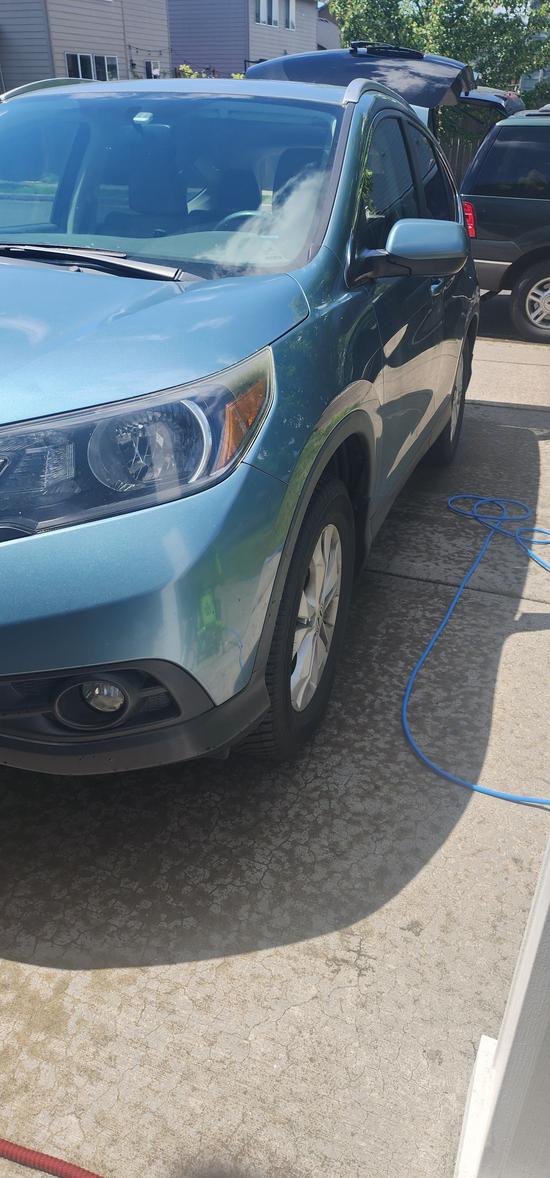A blue car is parked in a driveway next to a hose.