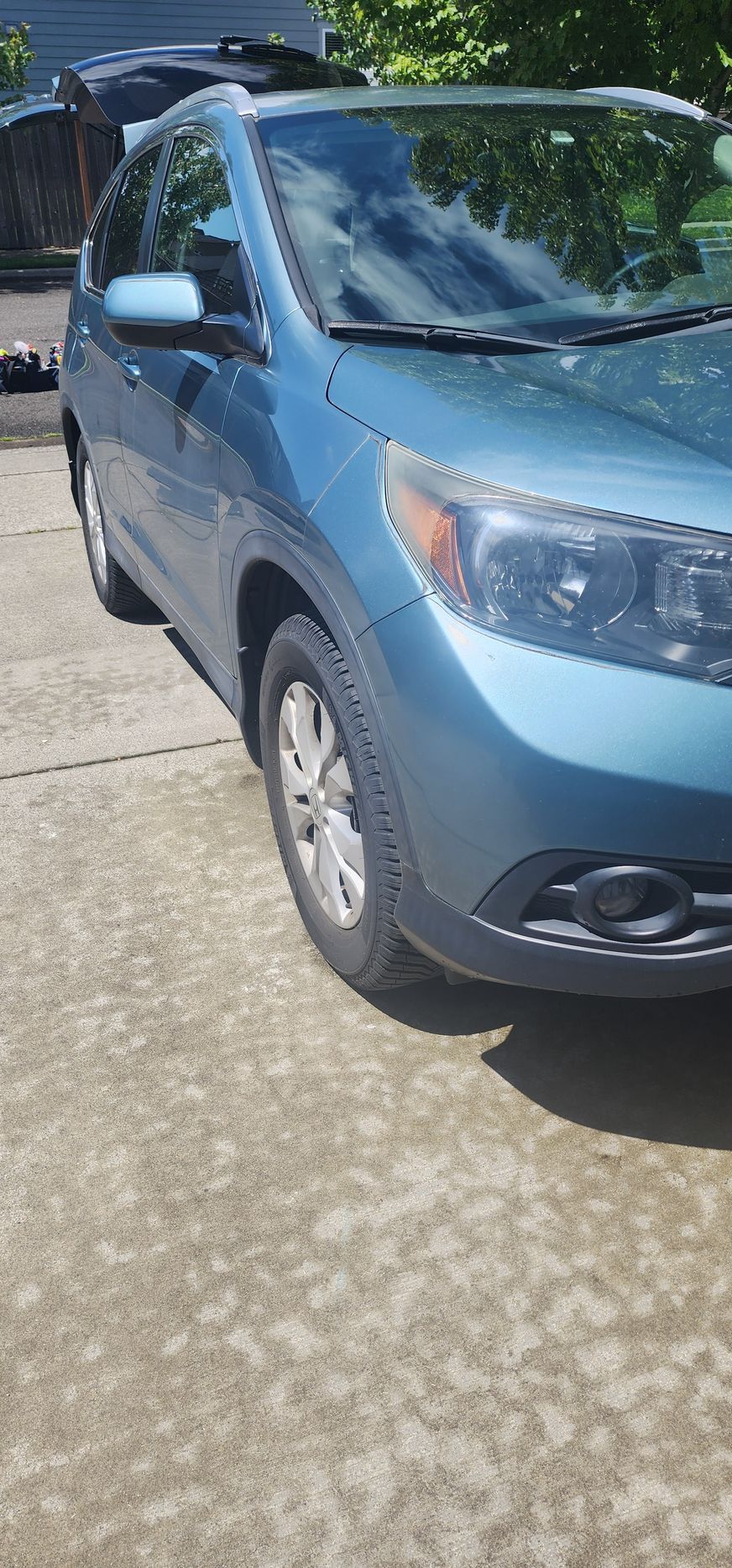 A blue car is parked in a driveway next to a house.