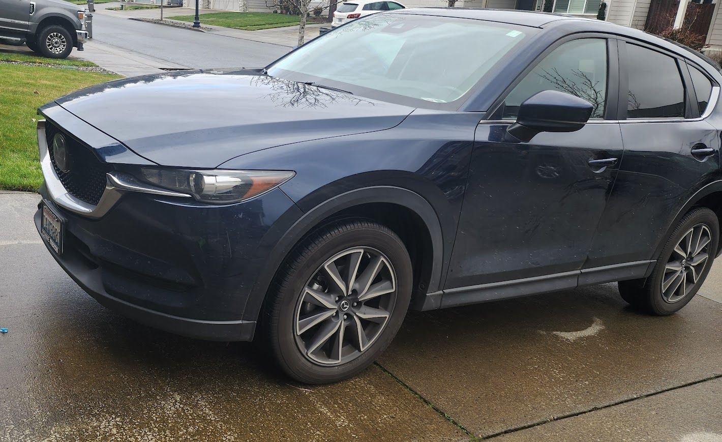 A blue mazda cx-5 is parked in a driveway on a rainy day.