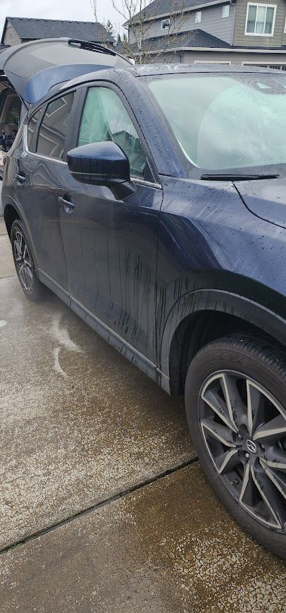 A blue car with the trunk open is parked on the side of the road.