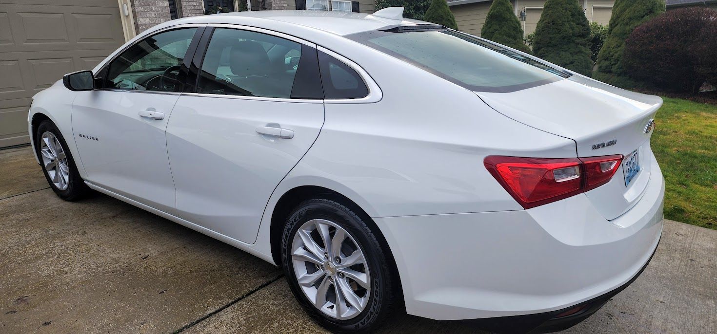 A white chevrolet malibu is parked in a driveway next to a garage.