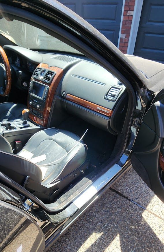 A black car with the door open is parked in front of a garage.