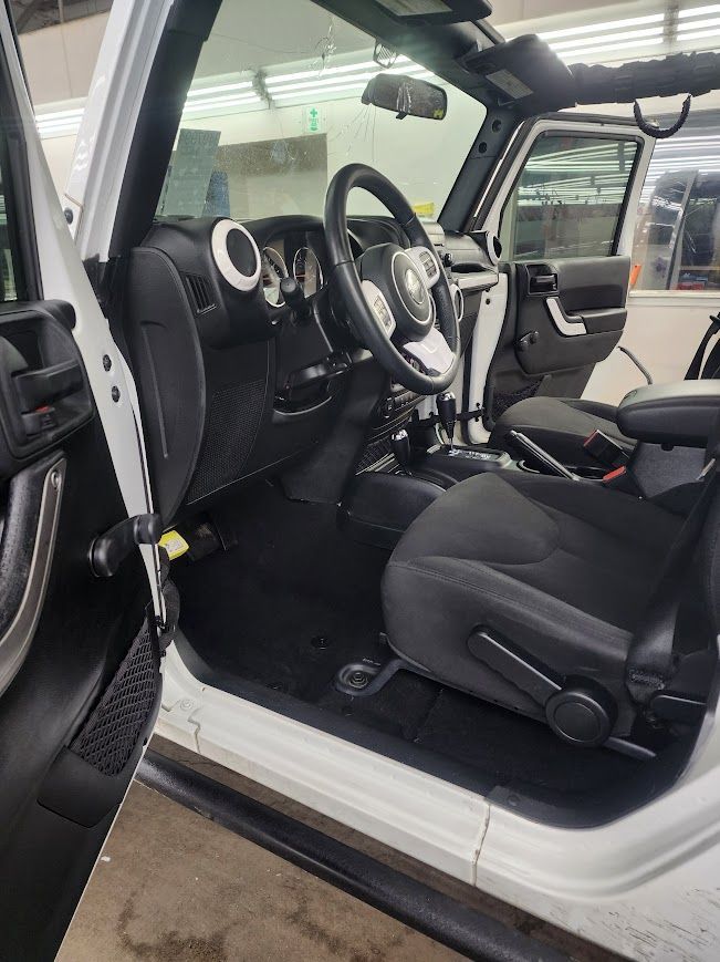 The interior of a white jeep wrangler with the door open.