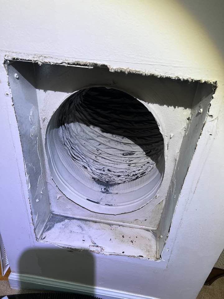 Damaged wall vent opening with exposed flexible duct inside a white wall