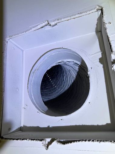 White square vent opening with a round duct hole in the center, set in a wall or ceiling panel.
