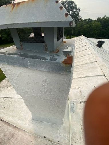 White rooftop chimney with rusted cap and vent, seen close-up on a sloped roof.