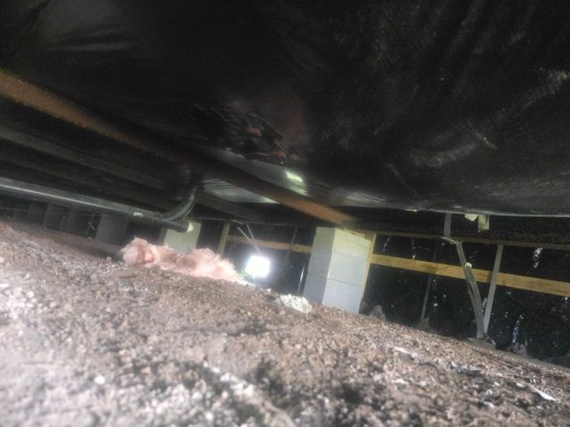Low-angle view of a crawlspace with dirt mound, beams, insulation, and a bright light in the background