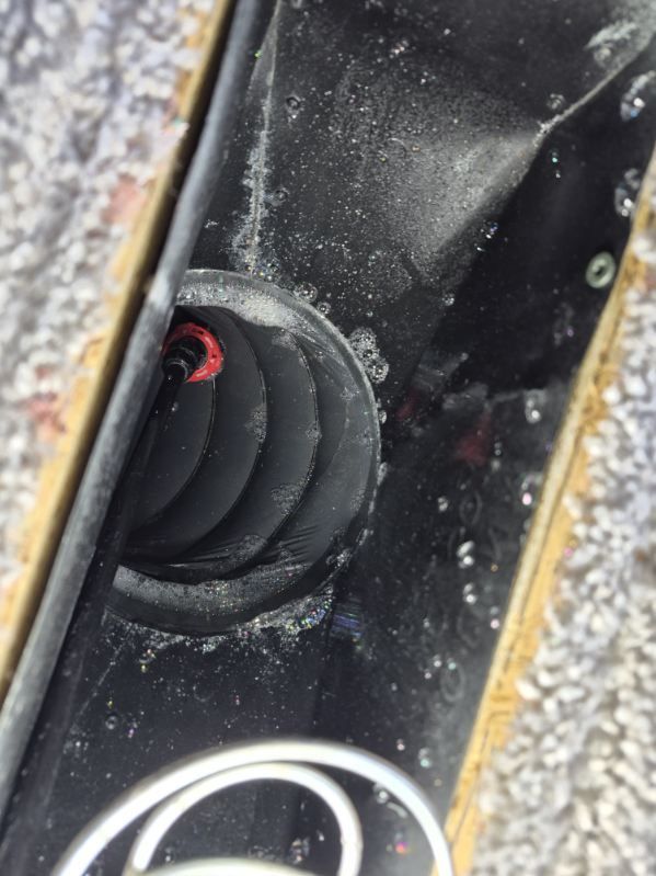 Close-up of a black device with a red coiled wire and white cable on gravel.