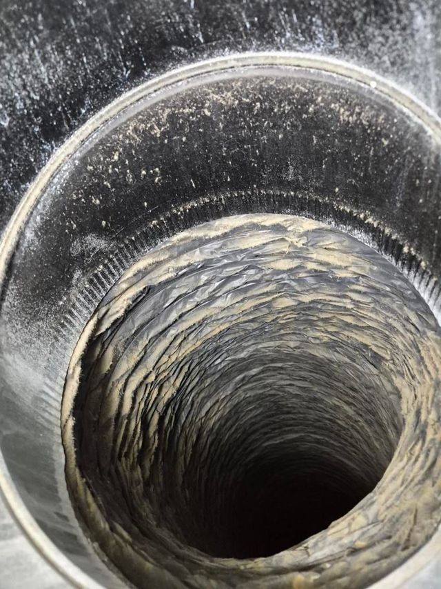 Close-up view down a dirty metal pipe with residue and a dark opening at the center