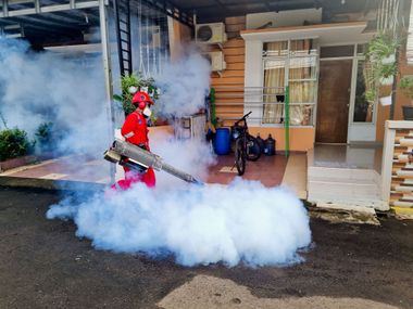 Person in red protective gear fogging a smoky residential doorway with a sprayer