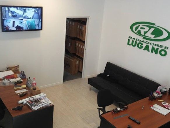 Pequeña oficina con escritorios, sofá negro, televisor de pared y el logotipo verde de