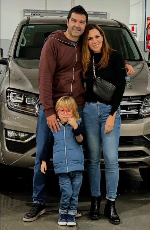 Una familia de tres personas posa frente a un SUV en un garaje, sonriendo y de pie muy juntos.