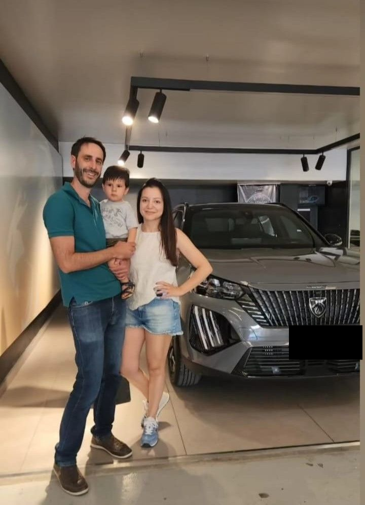 Una pareja posa en una sala de exposición junto a un SUV gris; el hombre abraza a la mujer y ambos sonríen.