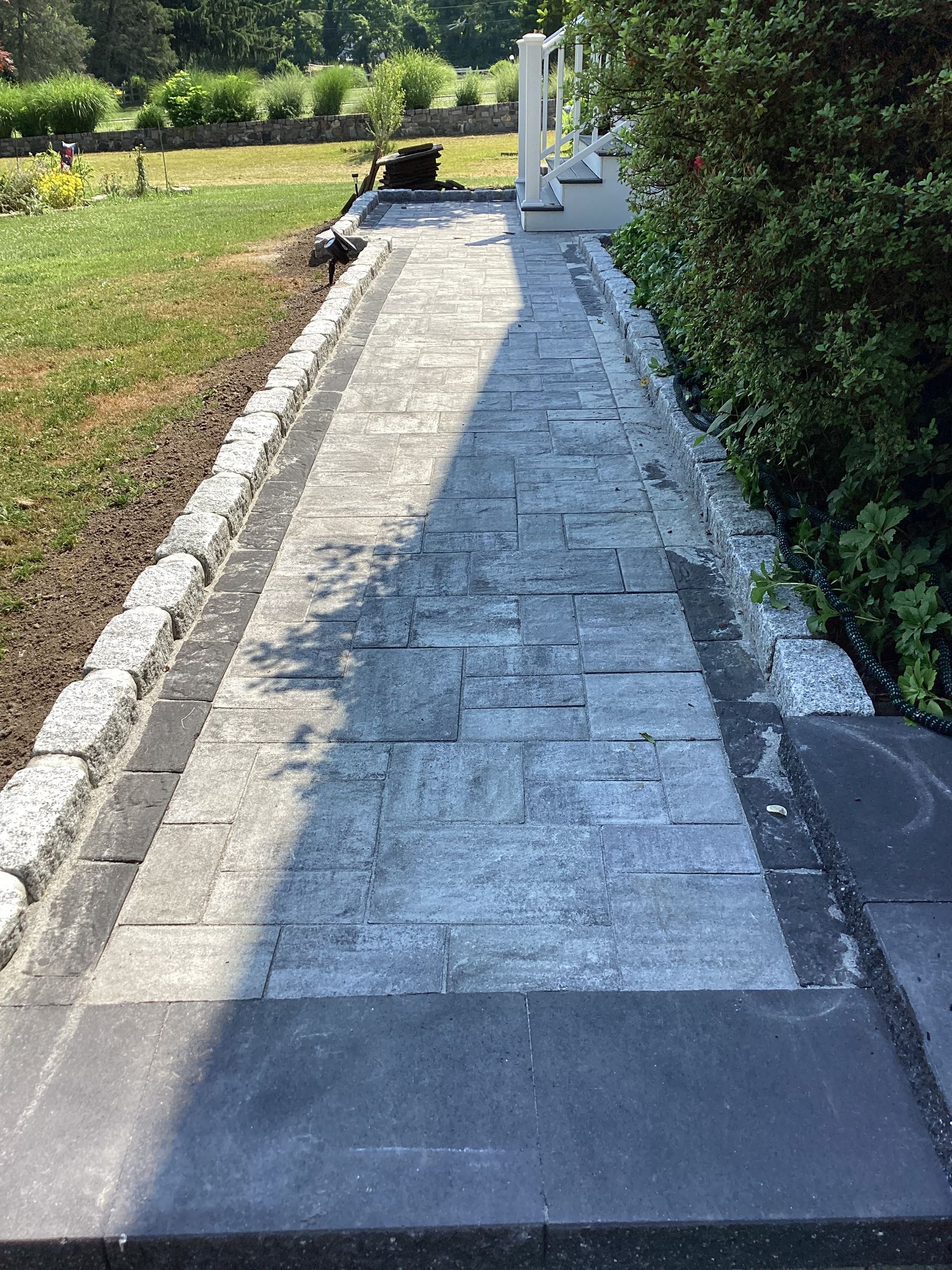 Stone walkway leading to a white porch with shrubs on one side and grass on the other.
