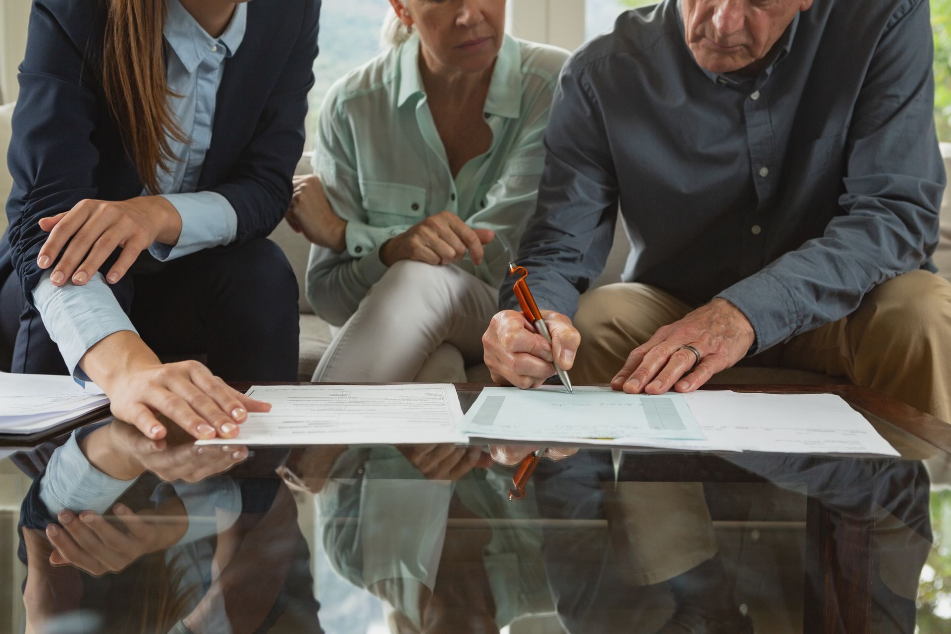 Person signing documents with two others present at a table.