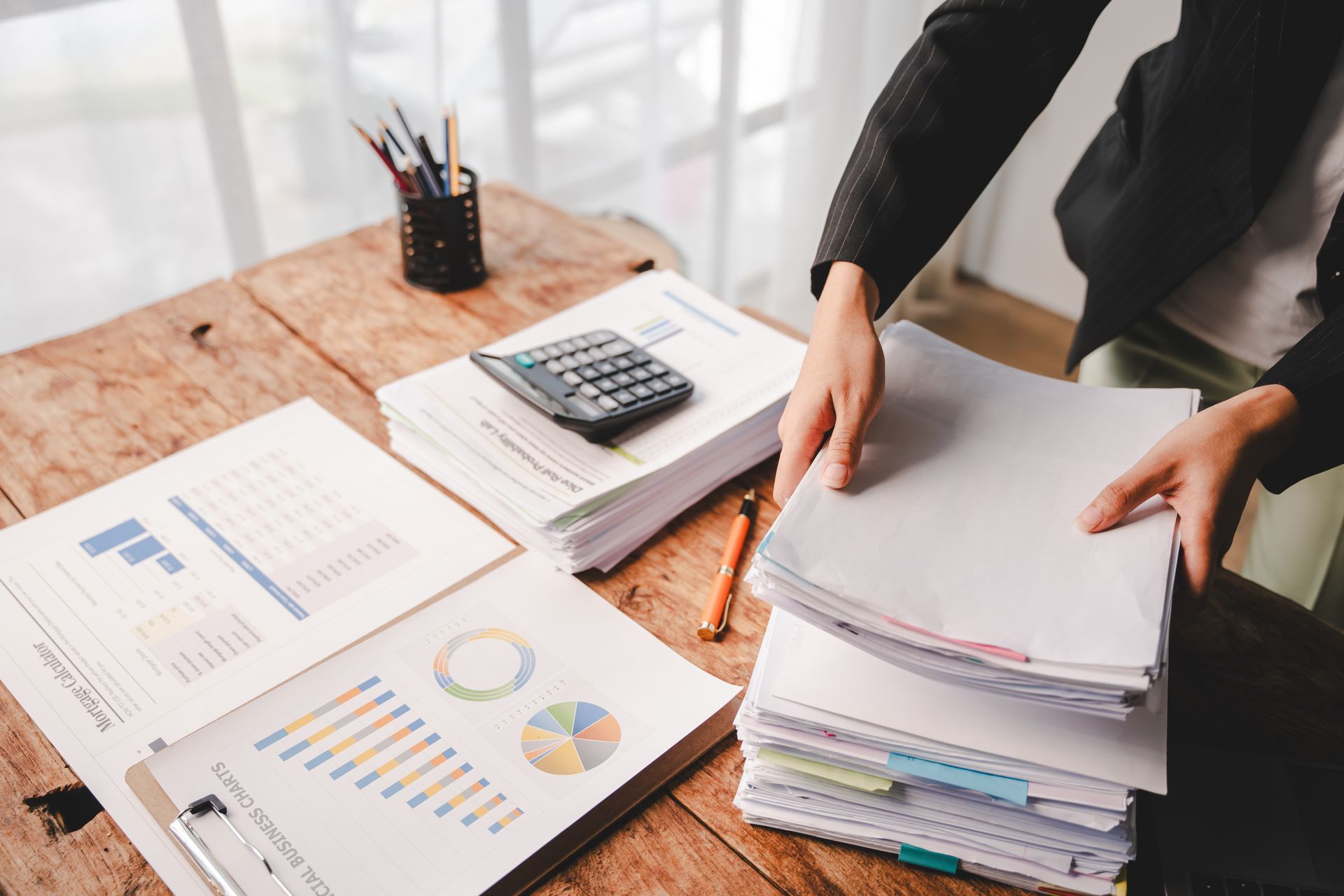 Person arranging paperwork on a wooden desk with charts, calculator, and pens.
