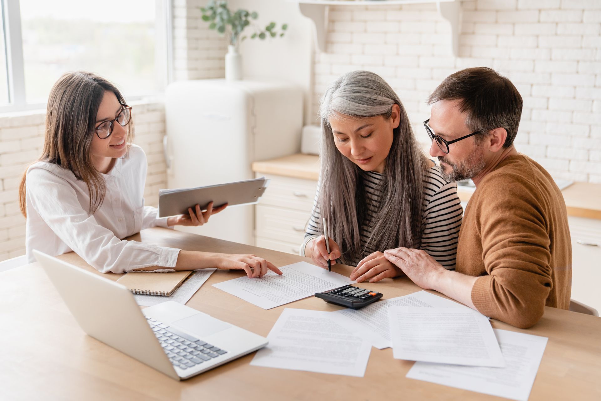 Woman advising couple, pointing to documents on table with laptop and calculator.