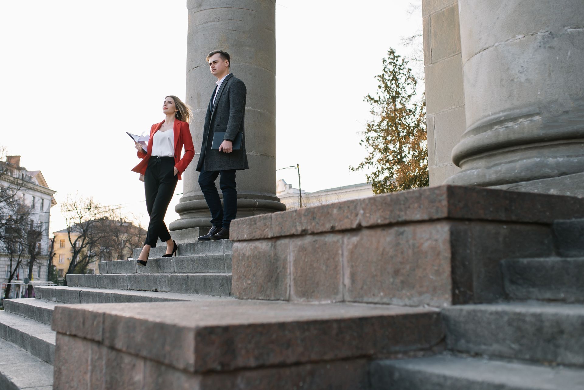 Woman and man in business attire descend stone steps of a building.