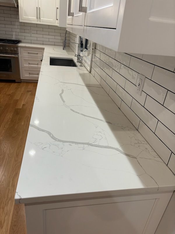 White kitchen with marble-look countertop and white subway tile backsplash, cabinets, and wood flooring.