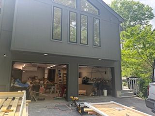 Gray two-story house with open garage under construction, tools and lumber visible inside and on driveway.