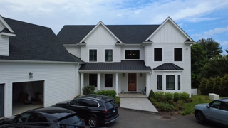 White two-story house with black shutters, front porch, driveway, and parked cars