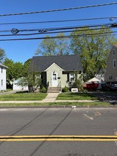 Small beige house with a black roof and front porch across a street on a sunny day