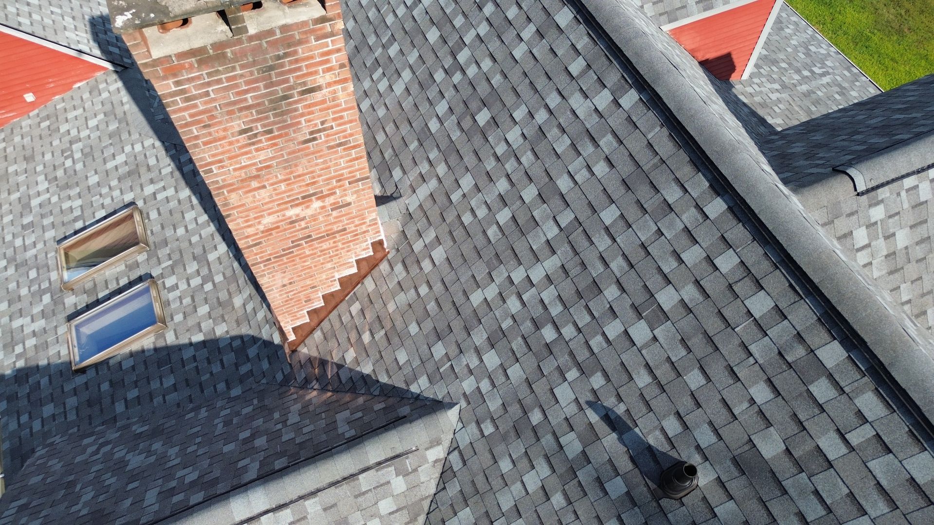 Close-up of overlapping gray and red roof shingles with skylights and chimneys on houses