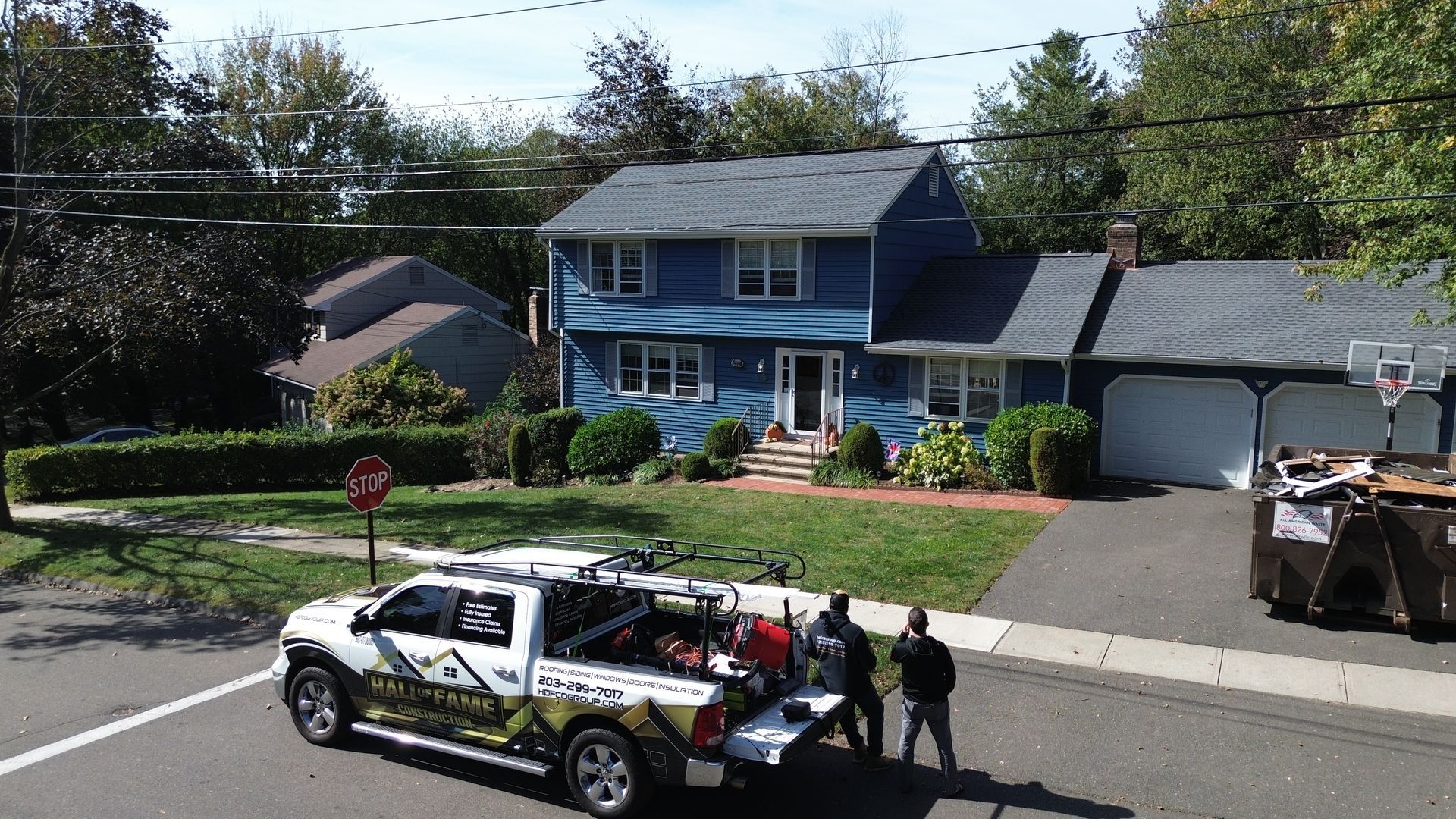 Tow truck on a suburban street in front of a blue house, loading a vehicle near a driveway.