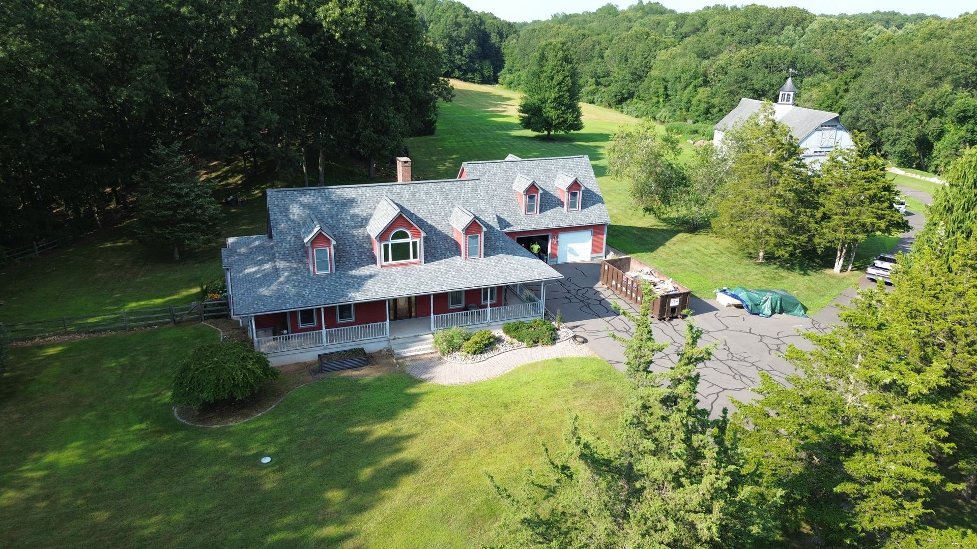 Aerial view of a large gray house with red dormers, surrounded by green trees and lawn.